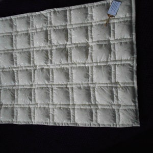May include: A white quilted blanket with a square pattern. The blanket is made of a soft, lightweight fabric and is perfect for cuddling up on the couch.