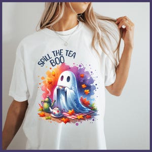 Pu&ograve; includere: Maglietta bianca con un design acquerellato colorato di un fantasma che tiene una tazza di t&egrave;. Il testo "Spill the Tea Boo" &egrave; stampato in nero sopra il fantasma.