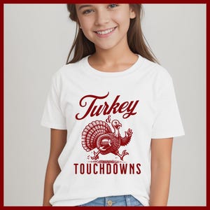 May include: White t-shirt with a red graphic of a turkey holding a football and the text "Turkey & Touchdowns".