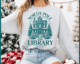 May include: A gray sweatshirt with a teal graphic of a house with snow on the roof and the text "North Pole Library" and "Reading is the best gift of all".