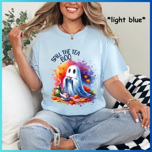 Pu&ograve; includere: Una maglietta blu chiaro con un'immagine di un fantasma che beve il t&egrave; e il testo "Spill the Boo Tea".