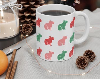 Può includere: Una tazza in ceramica bianca con un motivo ripetitivo di capibara verdi e rosa. La tazza è piena di caffè e c'è del vapore che sale.