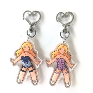 May include: Two clear acrylic keychains featuring cartoon figures with blonde hair and lingerie. One keychain has a blue corset design, and the other has a purple polka dot corset design. Each keychain has a silver heart-shaped clasp.