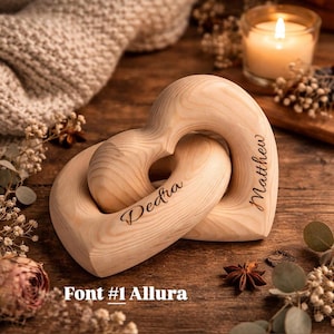 May include: Two interlocking wooden heart shapes, engraved with the names "Dedra" and "Matthew". The hearts are light-colored wood, with a natural grain. The text "Font #1 Allura" is at the bottom. The hearts are a romantic gift.