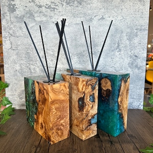 May include: Three wooden diffuser blocks with green and blue resin accents. Each block has black diffuser sticks inserted into the top.