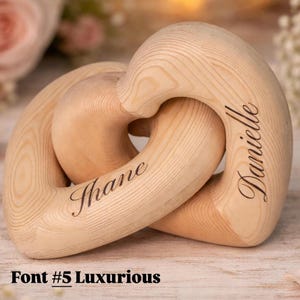 May include: Interlocking wooden heart-shaped rings with the names "Shane" and "Danielle" engraved in a cursive font. The rings are made of light-colored wood and are interlocked. The text "Font #5 Luxurious" is at the bottom.