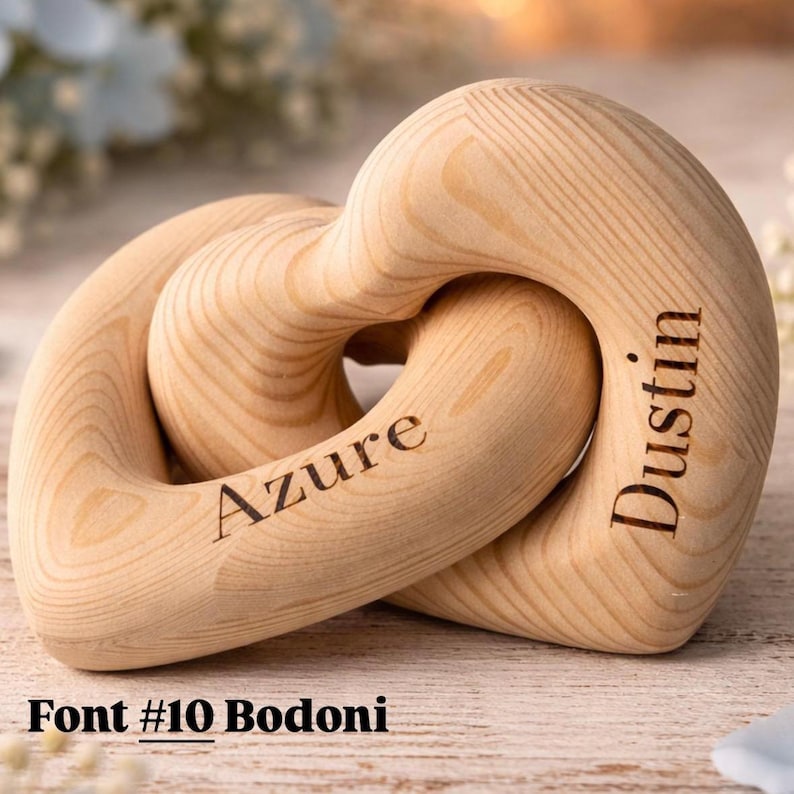 May include: A wooden heart-shaped sculpture with interlocking rings. The sculpture is light brown with the names "Azure" and "Dustin" engraved on it. The text "Font #10 Bodoni" is at the bottom.