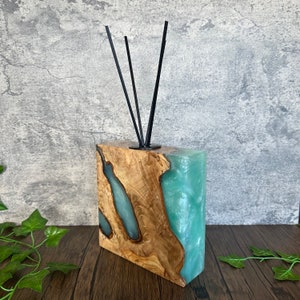 Puede incluir: Un difusor de madera y resina con un diseño de remolino azul claro y verde. El difusor tiene palitos negros para difundir aceites esenciales.