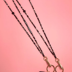 May include: Two black beaded necklaces with gold clasps and tassels. One necklace has the word "FIRST GRADE" spelled out in black beads. Both necklaces have a small black star charm.