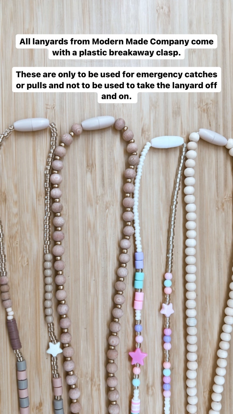 May include: Five wooden bead lanyards with different colored beads and charms. The lanyards are on a wooden surface. All lanyards from Modern Made Company come with a plastic breakaway clasp. These are only to be used for emergency catches or pulls and not to be used to take the lanyard off and on.