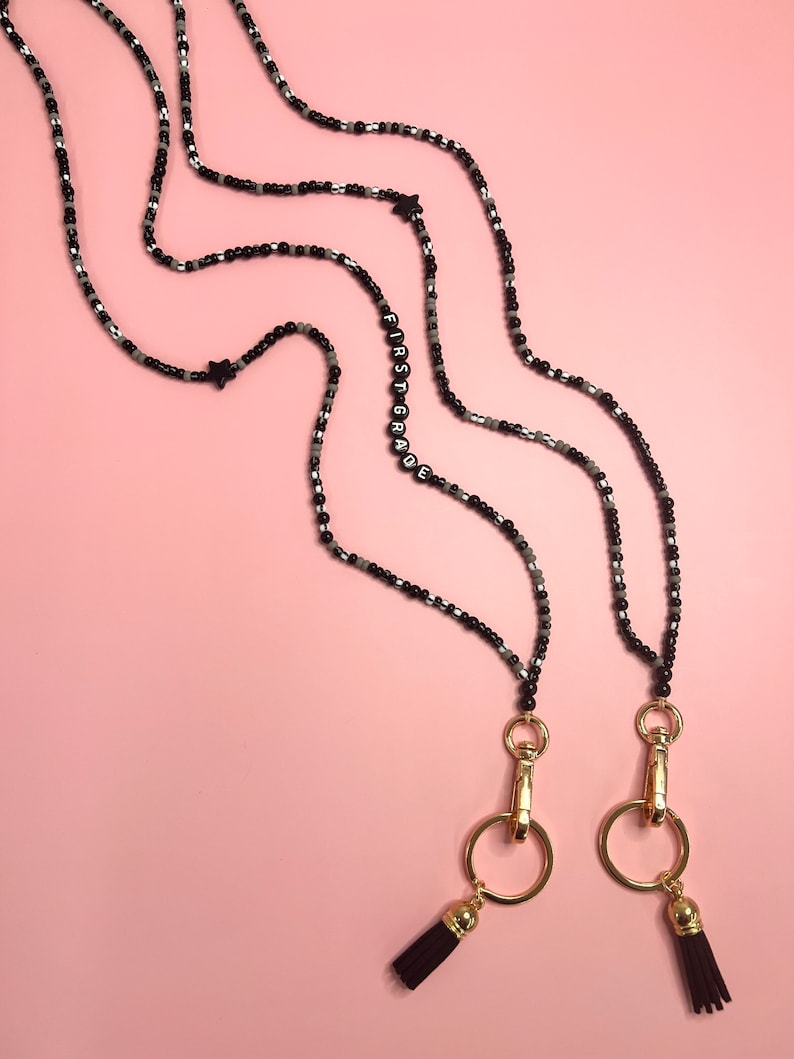 May include: Two black beaded necklaces with gold clasps and tassels. One necklace has the word "FIRST GRADE" spelled out in black beads.