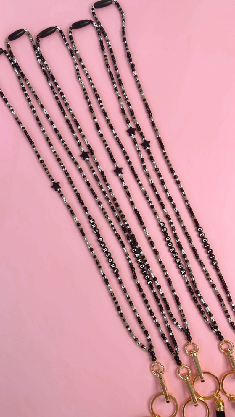 May include: Five black and white beaded lanyards with gold clasps and star charms. The lanyards have the names "Candice", "Msquezada", "Mrs Parsons", and "Cecilia" spelled out in black beads.
