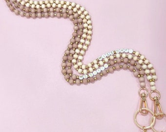 May include: A multi-strand beaded lanyard with gold-toned hardware and tassels. The beads are in shades of beige and brown, and the lanyard has the words "Miss Duff" and "Miss Britt" spelled out in white letters.