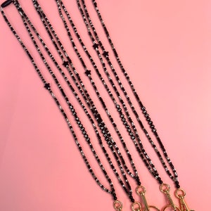 May include: Five black and silver beaded lanyards with gold clasps and black tassels. Each lanyard has a black star charm and a name spelled out in black beads: Cecilia, Ms. Quezada, Candice, Ms. Parsons.