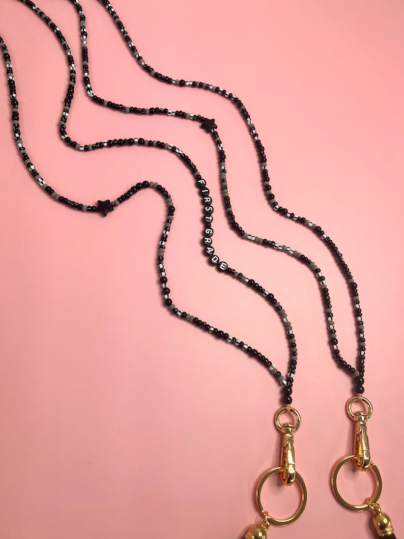 May include: Two black and white beaded lanyards with gold clasps. The lanyards have the word "FIRST GRADE" spelled out in black beads.