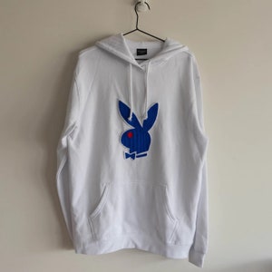 May include: White hooded sweatshirt with a blue Playboy bunny logo with a red eye and a white bow tie.