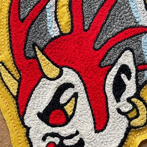 Puede incluir: Un parche bordado que muestra un personaje estilizado con una cresta roja brillante, piel blanca y un peque&ntilde;o cuerno amarillo. El dise&ntilde;o incluye contornos negros, detalles grises de fondo y acentos azul claro, bordeado con fieltro amarillo.