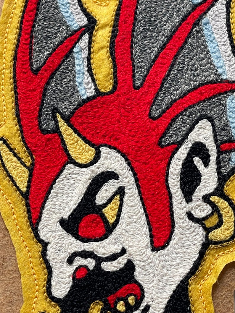 Puede incluir: Un parche bordado que muestra un personaje estilizado con una cresta roja brillante, piel blanca y un peque&ntilde;o cuerno amarillo. El dise&ntilde;o incluye contornos negros, detalles grises de fondo y acentos azul claro, bordeado con fieltro amarillo.