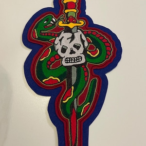 May include: Embroidered patch featuring a green snake coiled around a dagger, with a skull at the hilt. The design includes red, yellow, and black accents, set against a blue background. The patch is likely for clothing or accessories.