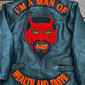 May include: Black leather jacket with a red devil face patch and a black patch that says "I'm a man of wealth and taste".