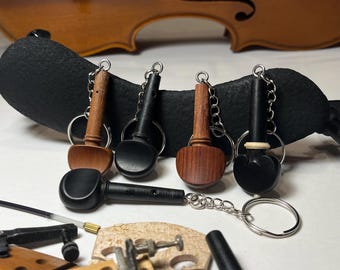 May include: Five wooden violin tuning peg keychains with silver key rings. The keychains are on a black violin shoulder rest.
