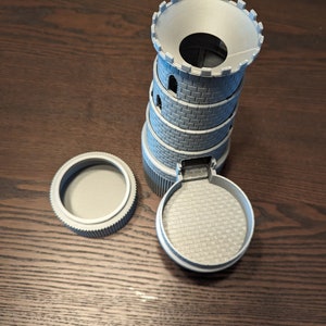 May include: A gray 3D printed tower with a round base and a removable top. The tower is made to look like a medieval castle with crenellations and windows.