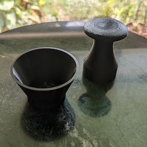May include: A black, 3D printed, cone-shaped cup and a black, 3D printed, mushroom-shaped object with a ridged top. Both objects are sitting on a dark green, marbled surface.