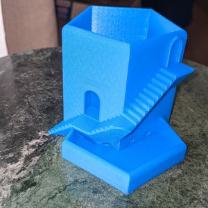 May include: A bright blue 3D printed planter shaped like a small house with a staircase leading to a doorway. The planter has a small, flat base.