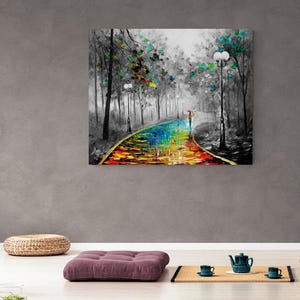 May include: A colorful oil painting depicts a path through a forest, with a person holding an umbrella. The path is a vibrant mix of rainbow colors, contrasting with the black and white trees and background. The artwork is displayed on a gray wall.