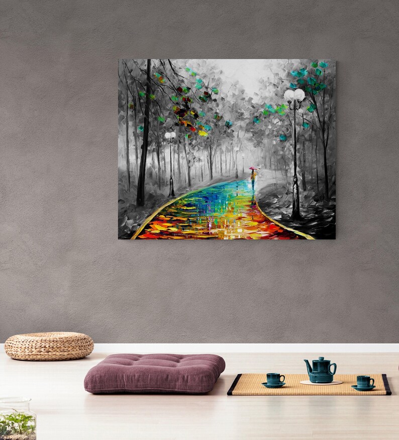 May include: A colorful oil painting depicts a path through a forest, with a person holding an umbrella. The path is a vibrant mix of rainbow colors, contrasting with the black and white trees and background. The artwork is displayed on a gray wall.