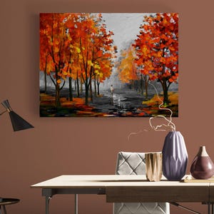 May include: An oil painting depicts a fall scene with trees in vibrant orange and yellow hues lining a path. A figure walks in the distance. The artwork is displayed on a brown wall, with a black lamp and decorative vases on a table in the foreground.
