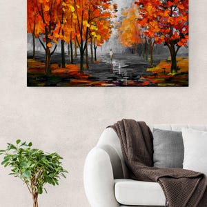 May include: An oil painting depicts a path lined with trees in autumn. The trees have vibrant orange and yellow leaves. A person walks down the path. The painting is displayed on a wall above a white sofa.
