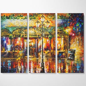 May include: A triptych canvas print of a vibrant cityscape at night. The artwork depicts a cafe with the name "CLARE" above the entrance, a lamppost, and reflections on a wet street. The color palette includes warm tones of orange, yellow, and red.