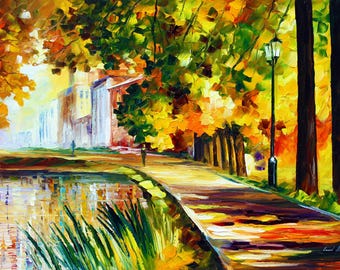 Op de afbeelding: Een impressionistisch olieverfschilderij van een parkscène in de herfst. Een pad leidt langs een vijver en bomen met gele en oranje bladeren. Op de achtergrond is een gebouw te zien en een lantaarnpaal staat langs het pad.