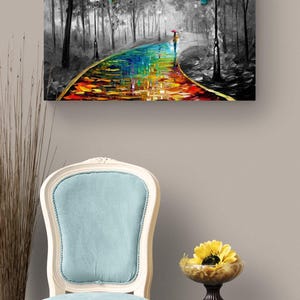 May include: Oil painting on canvas depicting a colorful path through a black and white forest. A person with an umbrella walks along the path. A light blue chair and a small table with a yellow flower are in the foreground.