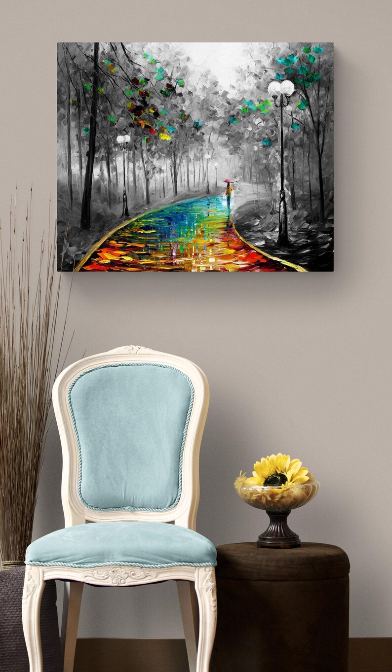 May include: Oil painting on canvas depicting a colorful path through a black and white forest. A person with an umbrella walks along the path. A light blue chair and a small table with a yellow flower are in the foreground.