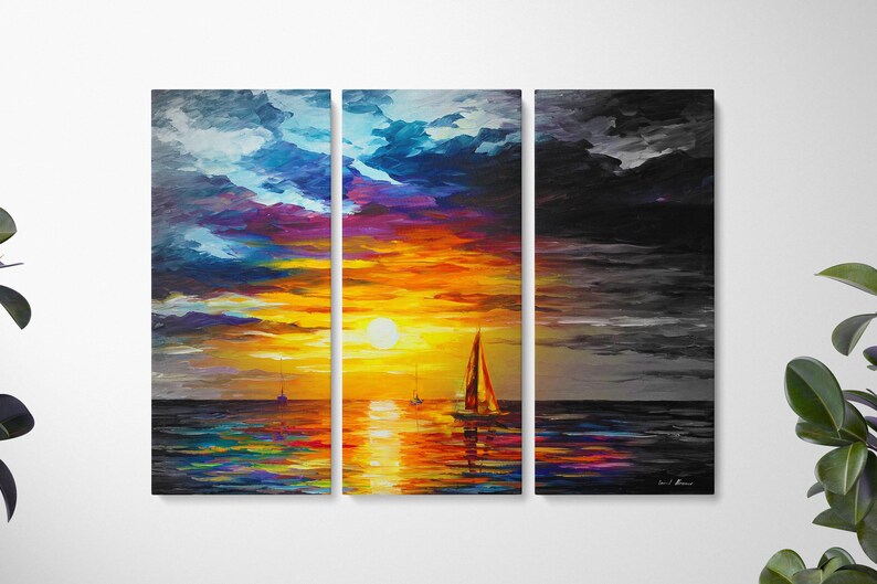 May include: A triptych canvas print depicting a sunset over the ocean. The sky transitions from blue and purple to vibrant orange and yellow, with a large sun. Sailboats dot the water, reflecting the colorful sky. The right panel is a grayscale version.
