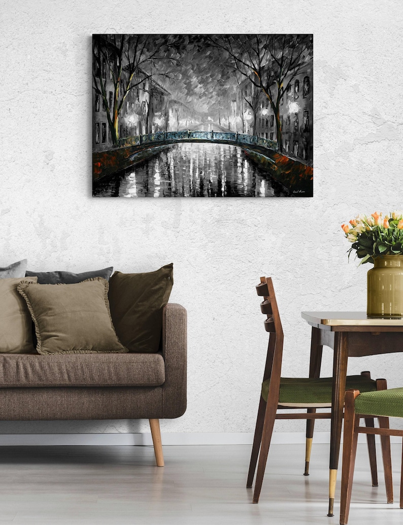 May include: A black and white painting of a bridge over a canal at night. The artwork depicts a European city scene with streetlights illuminating the water and buildings. The painting is displayed on a white wall.