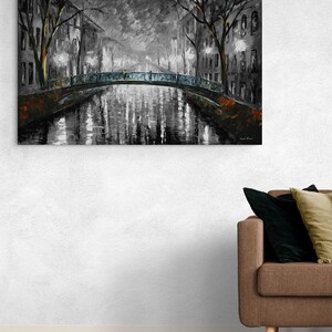 May include: A grayscale oil painting depicts a canal scene with a bridge and buildings. The bridge has a blue-green railing. Reflections of lights and buildings shimmer in the water. Bare trees frame the scene, adding a touch of nature to the urban landscape.