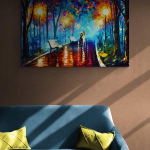 May include: An oil painting depicts a couple walking under an umbrella on a wet path in a park at night. The scene is illuminated by streetlights and features benches and colorful trees. The painting is displayed above a blue sofa with yellow pillows.