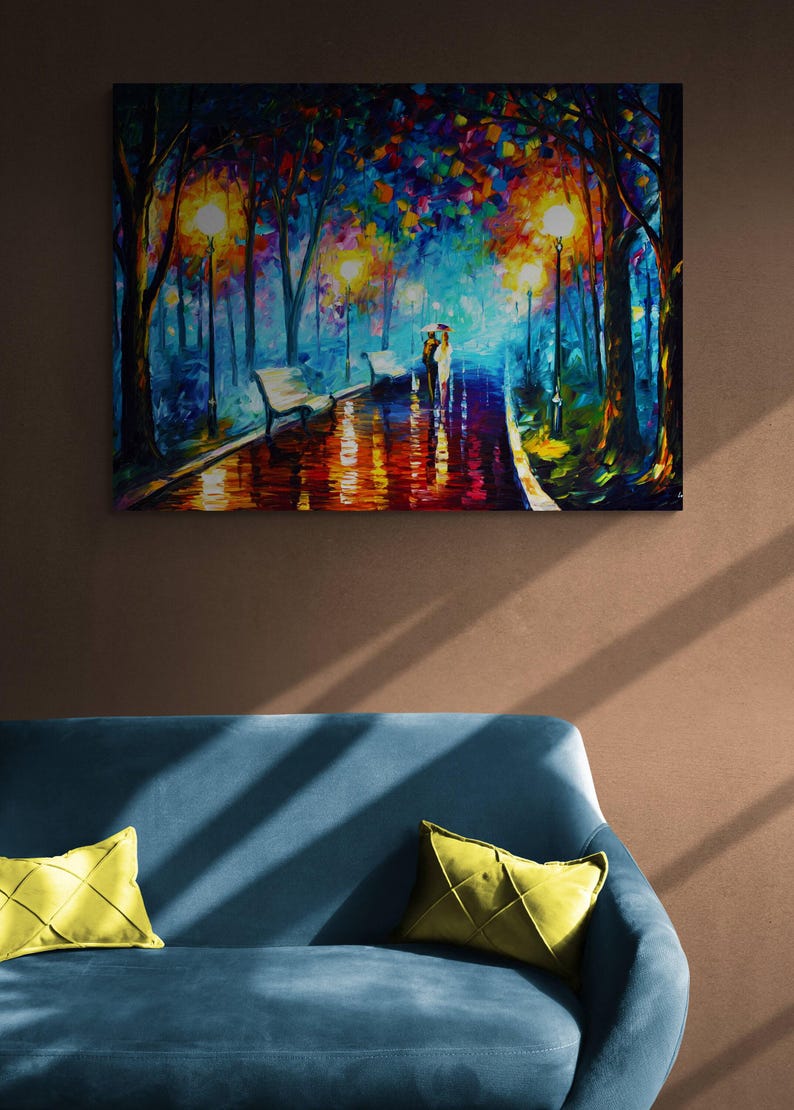 May include: An oil painting depicts a couple walking under an umbrella on a wet path in a park at night. The scene is illuminated by streetlights and features benches and colorful trees. The painting is displayed above a blue sofa with yellow pillows.