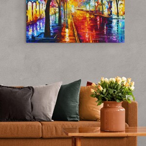 Pode incluir: Pintura a &oacute;leo de uma vibrante cena de rua noturna. A obra apresenta uma paleta colorida de vermelhos, laranjas, azuis e amarelos, com reflexos numa rua molhada. A pintura est&aacute; acima de um sof&aacute; castanho com almofadas e uma mesa de centro de madeira.