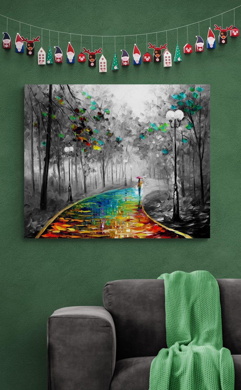 May include: A canvas print of a colorful, impressionistic landscape. A person with an umbrella walks along a vibrant, rainbow-colored path through a black and white forest. The artwork is displayed on a green wall, with a decorative garland above.