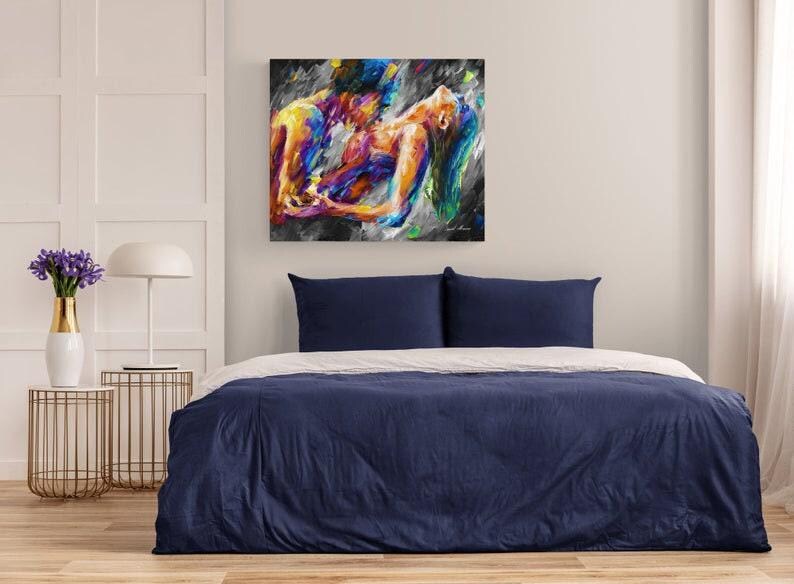 May include: Abstract painting of two figures embracing, rendered in vibrant hues of yellow, blue, orange, and purple against a dark background. The artwork hangs above a bed with a navy blue duvet and white sheets, creating a modern bedroom aesthetic.