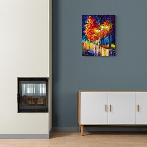 Peut inclure: Une peinture &agrave; l'huile color&eacute;e d'une sc&egrave;ne de rue nocturne. L'&oelig;uvre pr&eacute;sente des couleurs vives de rouge, orange, jaune et bleu, repr&eacute;sentant des arbres, des lampadaires et des reflets sur une surface mouill&eacute;e. La peinture est expos&eacute;e sur un mur bleu.