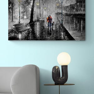 Puede incluir: Impresi&oacute;n art&iacute;stica en lienzo en blanco y negro que representa a una pareja paseando a un perro por una calle lluviosa. La obra de arte presenta farolas, &aacute;rboles y edificios, creando una escena rom&aacute;ntica y melanc&oacute;lica. La pintura se exhibe en una pared azul claro.