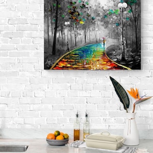 May include: A colorful oil painting depicts a path through a black and white forest. The path is a vibrant rainbow of colors, leading to a figure with an umbrella. The artwork is framed and mounted on a white brick wall.