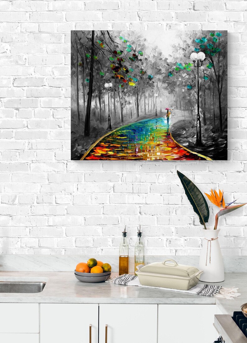 May include: A colorful oil painting depicts a path through a black and white forest. The path is a vibrant rainbow of colors, leading to a figure with an umbrella. The artwork is framed and mounted on a white brick wall.