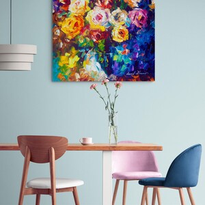 May include: An oil painting of a vibrant floral bouquet with yellow, orange, pink, and white roses against a dark blue background. The artwork hangs above a wooden table with chairs.