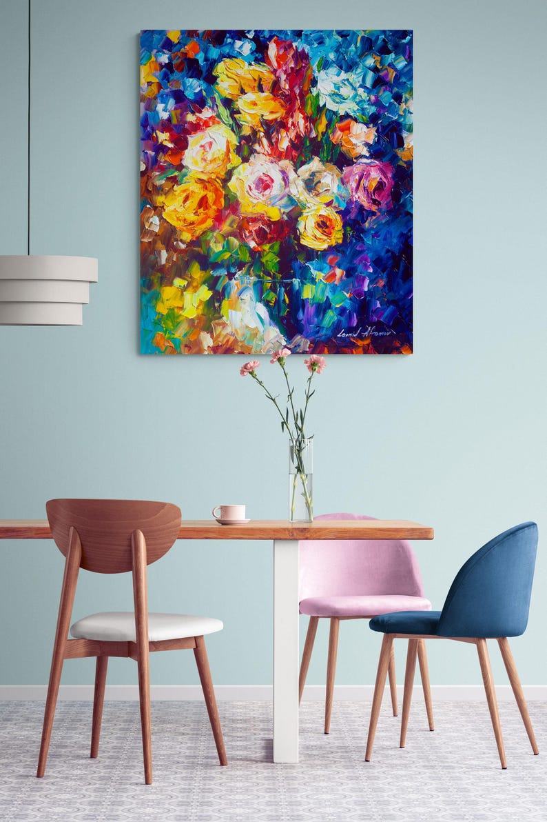 May include: An oil painting of a vibrant floral bouquet with yellow, orange, pink, and white roses against a dark blue background. The artwork hangs above a wooden table with chairs.